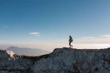 Yalnız bir yürüyüşçü, dağlarda açık bir günde gün batımında büyüleyici manzaranın tadını çıkararak kayalık bir tepeyi aşar..