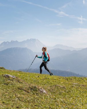 Bir insan açık bir günde çarpıcı bir dağ manzarasıyla çimenli bir arazide yürür, doğanın ve temiz havanın tadını çıkarır..