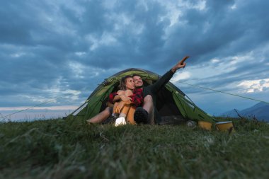 Alacakaranlıkta, çimenli bir tepede, bulutları işaret eden bir çadırda iki kişi birlikte oturur. Atmosfer rahat ve samimi..