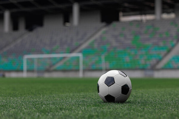 Футбольный мяч лежит на ухоженной зеленой траве пустого стадиона в дневное время.