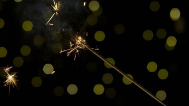 Siyah arka planda fıskiyeler yanıyor, şenlikli altın ışıklarla, yakın çekim. Mutlu yıllar konsepti.