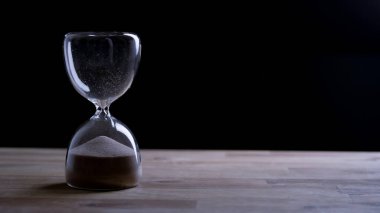 Kum saatinde siyah bir zemin üzerinde akan kum, zaman tükendi. Zamansızlık ve geçmiş kavramlar.