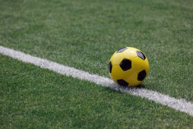 A yellow and black soccer ball sits by the sideline, ready for play on the well-kept stadium field.