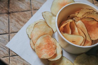 Taze ev yapımı kızarmış patates cipsi beyaz bir kutuda, ahşap tepside, üst manzaralı. Lezzetli bir yemek molası ve parti filmi için masaya serpiştirilmiş tuzlu cipsler..