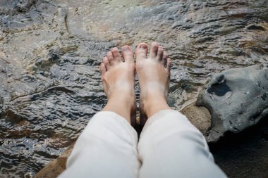 Tayland 'da şelale, tatil ve yaz konseptlerinde, bir dağ akıntısının berrak sularında oynarken ve eğlenirken ayaklarım daldı..