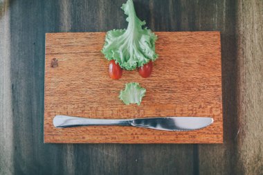 Taze sebzeler, tahta bir kesme tahtasının üzerinde kızgın bir yüz ifadesi oluşturdu..