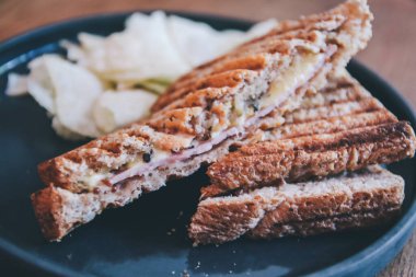 Kahvaltıda siyah tabakta jambon, peynir ve patates cipsi ile sağlıklı sandviç tostu..