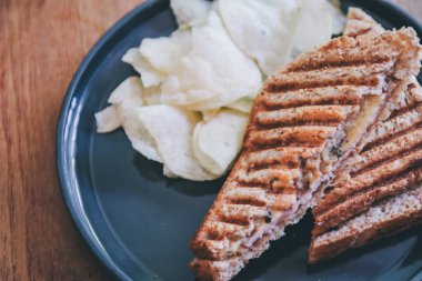 Kahvaltıda siyah tabakta jambon, peynir ve patates cipsi ile sağlıklı sandviç tostu..