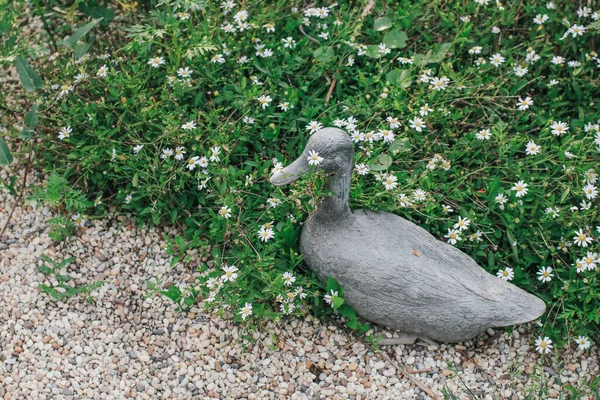 Ceramic cute duck next to a flowerbed. Decor Garden With Vintage stone duck statues for the outdoor garden decoration.