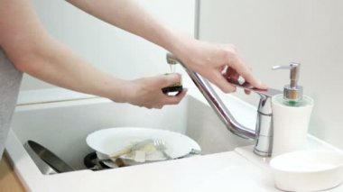 Kadın mutfağa sabun süngeri, bıçak, çatal ve plastik kaşık uzatıyor. Bulaşık yıkama rutini.