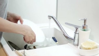 Kadın mutfakta sabun beyazı tabağı veriyor. Bulaşık yıkama rutini.