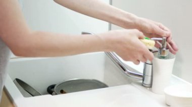 Kadın mutfağa sabun süngeri ve beyaz tabak uzatıyor. Bulaşık yıkama rutini.