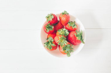 Beyaz ahşap bir masada taze çilek manzarası, yenmeye hazır bir kasenin içinde, organik ve sağlıklı yiyecek olarak.