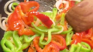 Yakın çekim, taze kırmızı ve yeşil biberli, tavada soğan sotelenmiş, ahşap bir spatulayla karıştırılmış, sağlıklı yemek, konsept, 4k