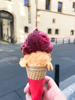 Elinde pembe ve turuncu kıvrımlı dondurma külahı tutan biri. Koni kırmızı ve beyaz.