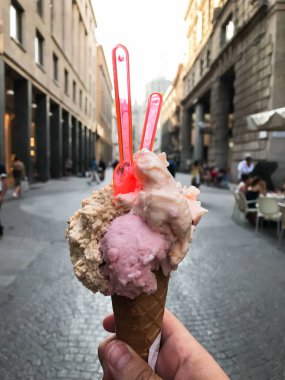 Elinde pembe ve turuncu kıvrımlı dondurma külahı tutan biri. Koni kırmızı ve beyaz.