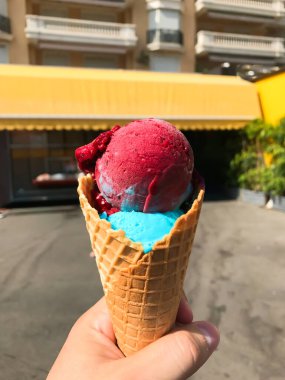 Elinde pembe ve mavi kıvrımlı dondurma külahı tutan biri. Koni