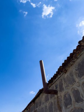 Baca, şömine borusu. Metal bir boru binadan dışarı çıkıyor. Gökyüzü mavi ve berrak. Boru paslanmış.