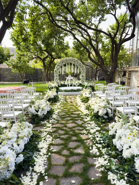Açık havada bir düğün, bahçede güzel beyaz bir düğün töreni düzenleniyor. Tören beyaz çiçeklerle süslenmiş beyaz bir kemerin altında yapılır ve sandalyeler kemerin etrafına dizilir.
