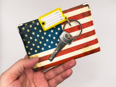 Keys, door kyes, home keys, mortgage in the USA, apartment for rent in the US, housing, buying a house in the USA, apartment mortgage, house rental loan. US flag, dollars. A hand holding a key with yellow keychain