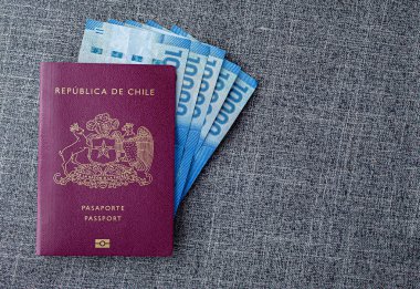 Gri kumaş bir masanın üzerinde Şili pezosu olan bir Kızıl Şili pasaportu.