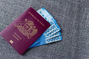 Gri kumaş bir masanın üzerinde Şili pezosu olan bir Kızıl Şili pasaportu.