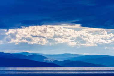 Baykal Gölü'nde bir fırtına sırasında mavi manzara, dağların siluetleri ve bulutlar güzel güneş tarafından aydınlatılmış