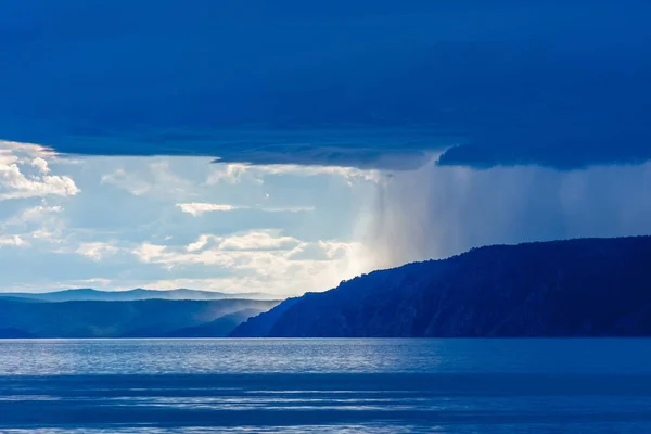 Storm cloud over lake Baikal with sun light and rain. Mountains in the fog, waves on the water, clouds and blue tones of the landscape