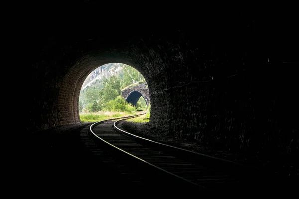Ljus med ett landskap i slutet av en sten järnvägstunnel med vackert upplysta skenor i fjällen Stockbild