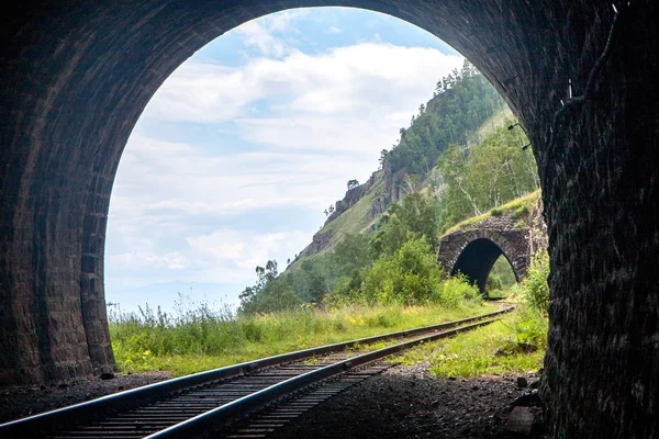 Ljus med ett vackert landskap i slutet av en sten järnvägstunnel i fjällen Stockbild