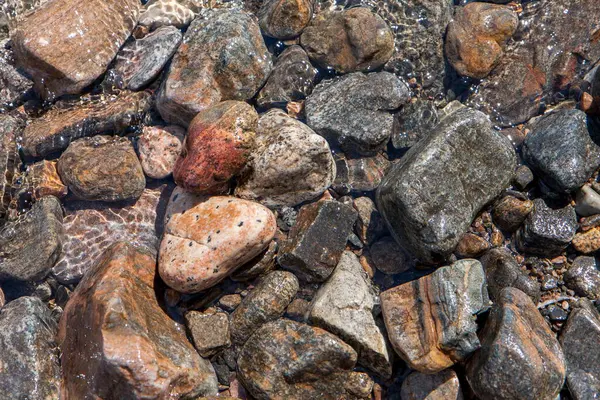 Sahilde kayalar ve çakıl taşları suda, çeşitli renklerde.