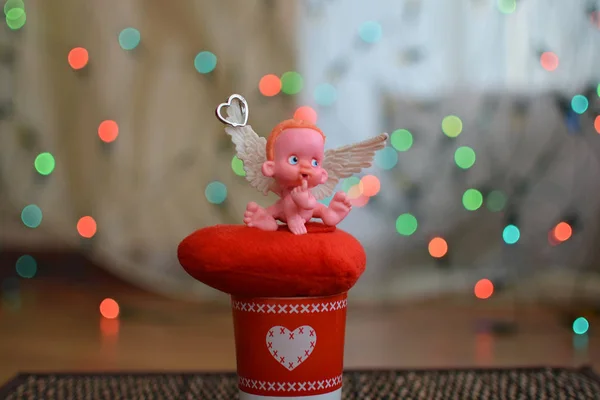 A small figure of an angel sitting on or near a jewelry box close up, a background bokeh of twinkling party lights — ストック写真