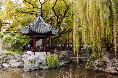 İnsanlar rahatlatıcı bir ahşap köşk arasında sarı yapraklar Shanghai Çin'Yu bahçesinde