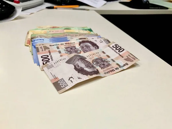 Muitas contas de peso mexicanas mistas espalhadas por uma mesa bege — Fotografia de Stock