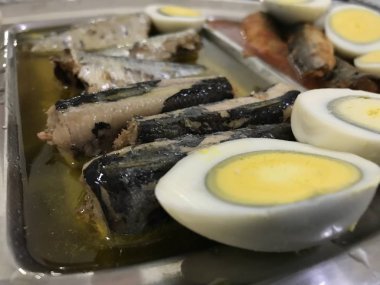 Mavi damalı masa örtüsü üzerine yerleştirilen paslanmaz çelik tepside yarıya, sardalye ve ton balığında kesilmiş pişmiş yumurta