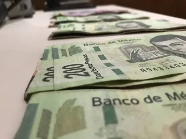 Many mexican pesos bills distributed and spread on a beige colored desk — Stock Photo, Image