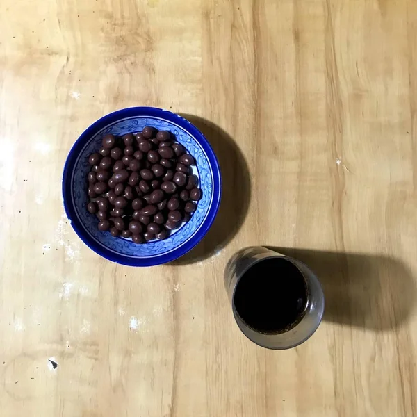 Tazza con uvetta ricoperta di cioccolato e bicchiere d'acqua sul tavolo di legno — Foto Stock