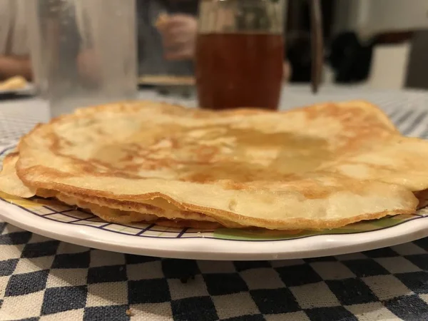 Vista lateral de un plato con una pila de crepes con un vaso de agua y miel en el fondo — Foto de Stock