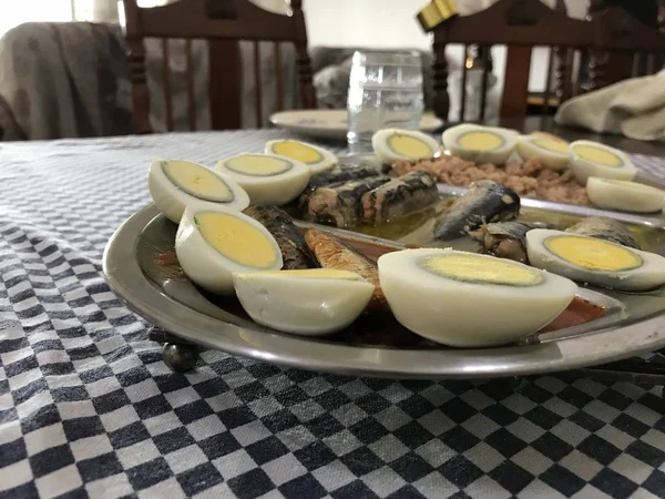 Œuf cuit coupé en deux, sardines et thon sur un plateau en acier inoxydable placé sur une nappe à carreaux bleus — Photo