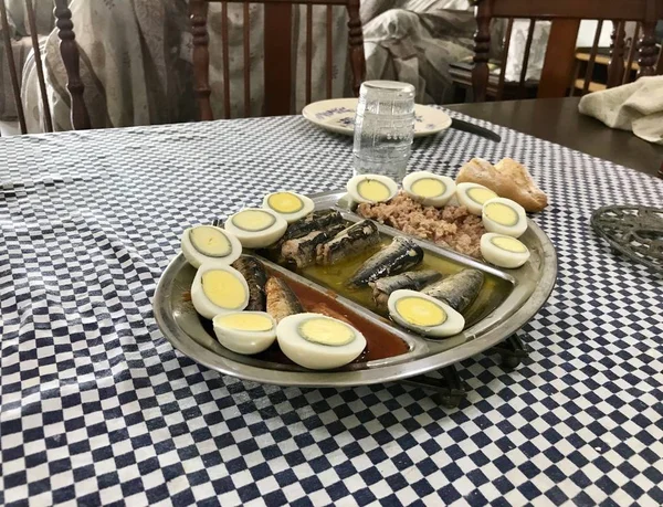 熟鸡蛋切成两半，沙丁鱼和金枪鱼放在一个不锈钢托盘上，放在蓝色格子桌布上 — 图库照片