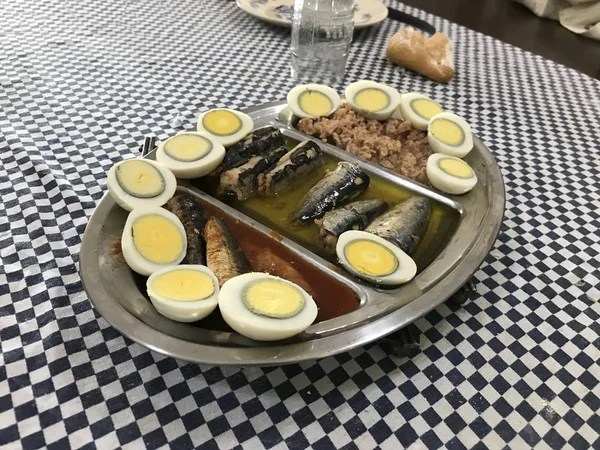 Œuf cuit coupé en deux, sardines et thon sur un plateau en acier inoxydable placé sur une nappe à carreaux bleus — Photo