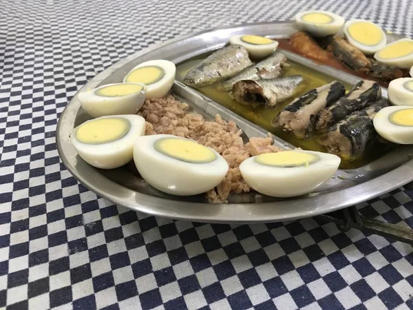 Œuf cuit coupé en deux, sardines et thon sur un plateau en acier inoxydable placé sur une nappe à carreaux bleus — Photo