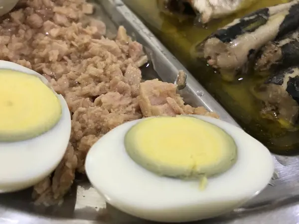 Œuf cuit coupé en deux, sardines et thon sur un plateau en acier inoxydable placé sur une nappe à carreaux bleus — Photo