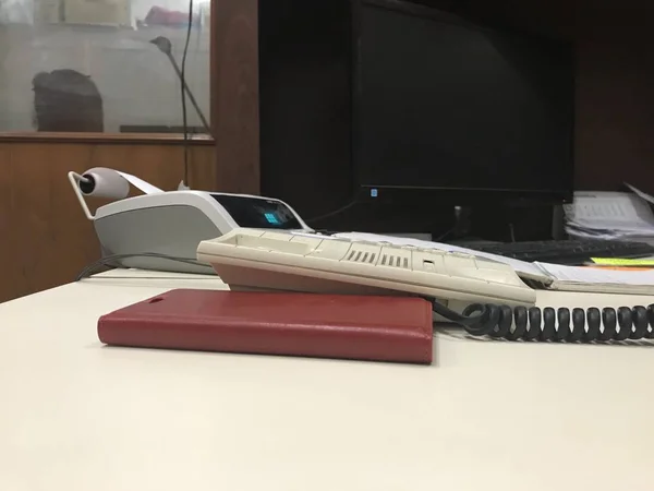 Mesa de escritório com telefone fixo, carteira de couro vermelho, calculadora e monitor de computador em cima dela — Fotografia de Stock