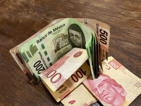 Many mixed Mexican peso bills spread over a wooden desk — Stock Photo, Image