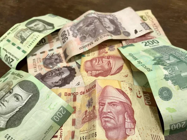 Many mixed Mexican peso bills spread over a wooden desk — Stock Photo, Image