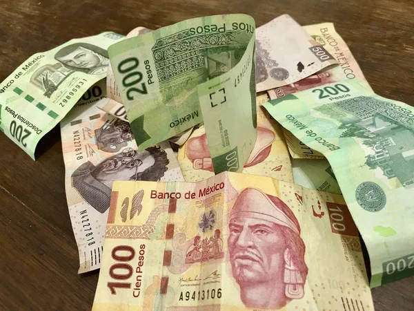 Muchos billetes mixtos de peso mexicano repartidos sobre un escritorio de madera — Foto de Stock