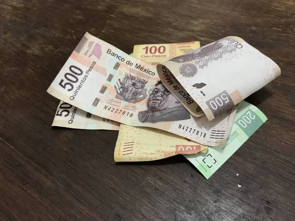 Muitas contas de peso mexicanas mistas espalhadas por uma mesa de madeira — Fotografia de Stock