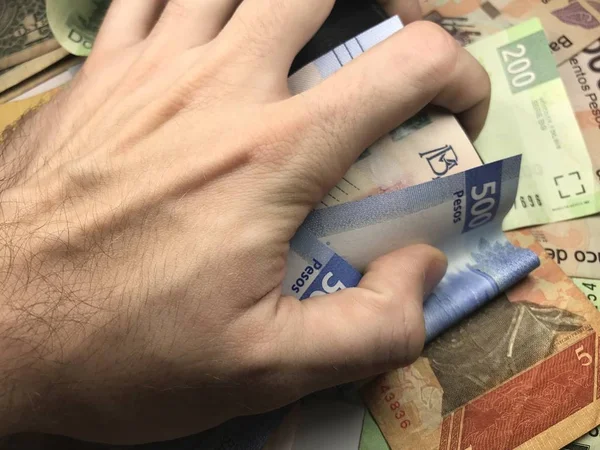 Τα χαρτονομίσματα του Μεξικού εξαπλώνονται τυχαία πάνω από μια επίπεδη επιφάνεια με ένα χέρι πάνω τους. — Φωτογραφία Αρχείου