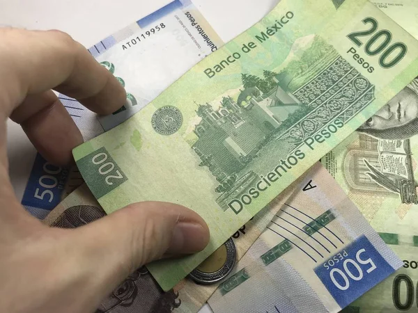 Billetes de pesos mexicanos distribuidos al azar sobre una superficie plana con una mano sobre ellos — Foto de Stock